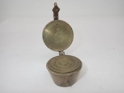 une vieille casserole en laiton avec un couvercle, posée sur une surface blanche