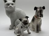 three figurines of dogs and a cat on a white background