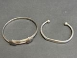 two silver bracelets and a silver bang on a table