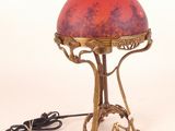 brass table lamp with a red shade and a cord plugged into the base