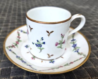 une tasse et une soucoupe blanches à bord doré posées sur une table