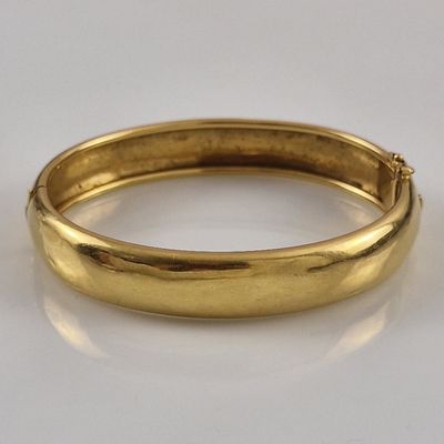 a close up of a gold bang bracelet on a white surface