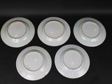 four white plates with gold rims on a black surface