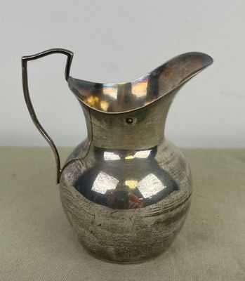 une cruche en métal plaqué argent, dotée d'une anse recourbée, posée sur une table
