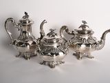 four pieces of silver tea and coffee set on a white surface