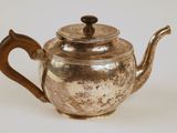 une théière en argent avec une poignée en bois posée sur une surface blanche