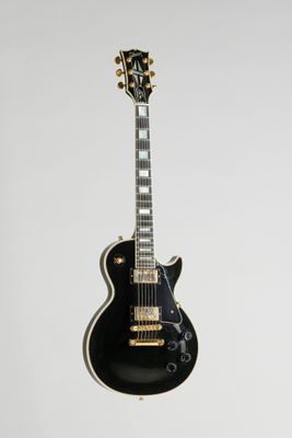 a black electric guitar hanging from a white wall