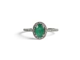 a close up of a ring with an oval emerald stone surrounded by diamonds