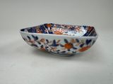 an orange and blue bowl with flowers on it on a white surface