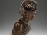 bronze bust of a boy on a wooden base on a gray background