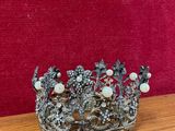 une couronne en métal argenté ornée de perles et de fleurs, posée sur une table en bois