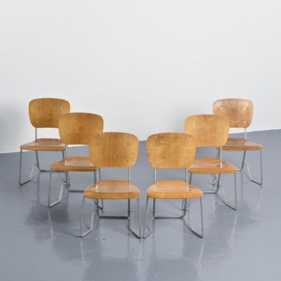 Quatre chaises en bois sont disposées en cercle sur un sol gris.