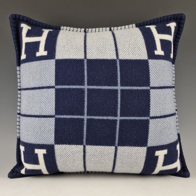 un coussin à carreaux bleus et blancs sur lequel figure la lettre h