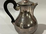 a silver coffee pot with a black handle on a white surface