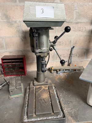 une perceuse posée sur une table dans une pièce où se trouvent de nombreux outils
