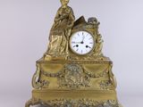 a gold clock with a woman sitting on top of it