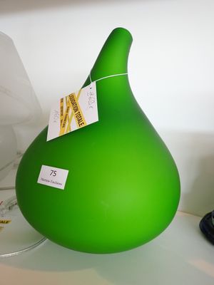un vase vert posé sur une étagère blanche, à côté d'un verre