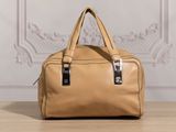 a tan handbag sitting on top of a wooden table next to a wall