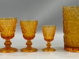 five glasses and a pitcher sitting next to each other on a table