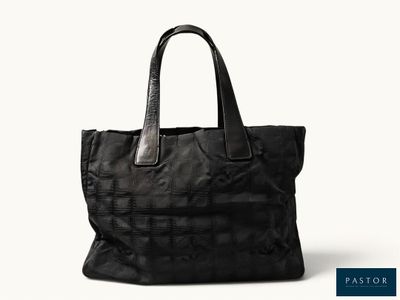 le grand sac fourre-tout noir est posé sur une surface blanche