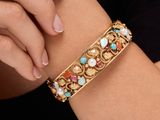 a close up of a woman ' s arm wearing a gold bracelet with multi colored stones