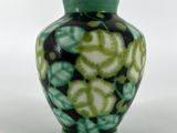 un vase vert et noir posé sur une surface blanche