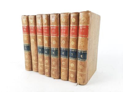 six old books are lined up on a white surface