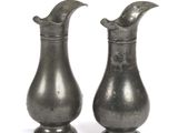 two silver vases sitting next to each other on a white surface