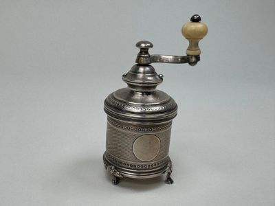 un moulin à café ancien en argent, surmonté d'une petite lampe jaune