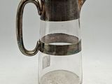 un pichet en verre muni d'une anse en métal, posé sur une table