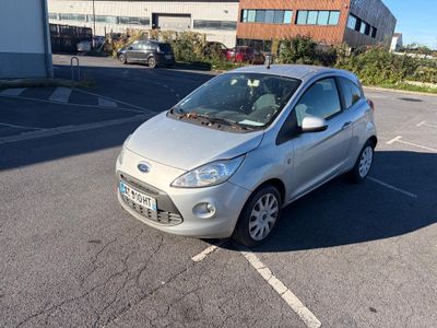 La petite voiture argentée est garée sur un parking près d'un immeuble.