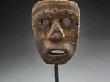 un masque en bois posé sur un socle, sur une surface grise
