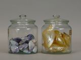 two glass jars with shells in them on a table