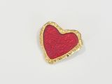 une broche en forme de cœur rouge, bordée d'or, sur fond blanc