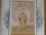 an old picture of a young boy in a red dress sitting in front of a framed picture