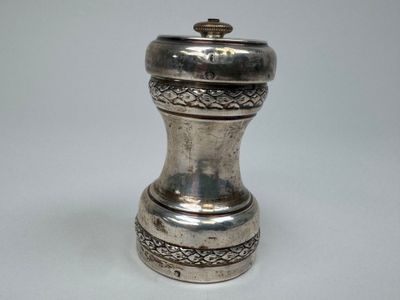 une poivrière en argent posée sur une surface blanche