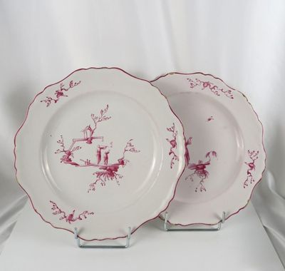 two plates with red and white designs on them sitting on a white surface