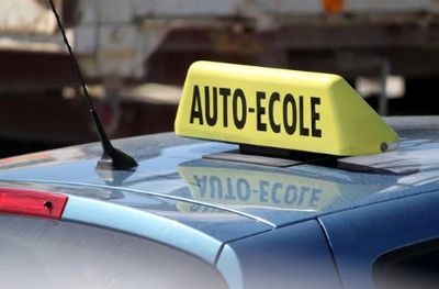 une enseigne « taxi » posée sur le toit d'une voiture, sur laquelle on peut lire « auto-école »