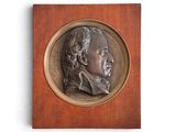 une image représentant un médaillon en bronze à l'effigie d'un homme, monté sur une plaque en bois