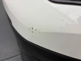 the front bumper of a white car with a hole in it