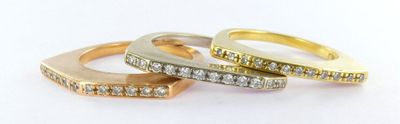 three gold and diamond rings on a white surface