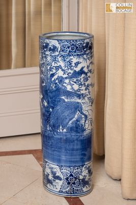 un vase bleu et blanc posé par terre devant un rideau