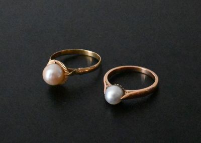 two gold rings with pearls on them on a black surface