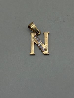 a close up of a gold pendant with a letter n on it