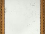 un miroir ancien dans un cadre doré, accroché à un mur blanc, avec un bout de papier