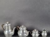 trois théières en argent et une cafetière posées sur une table