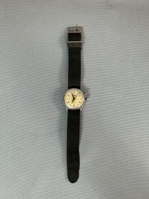 La montre repose sur une surface blanche et est dotée d'un bracelet noir.