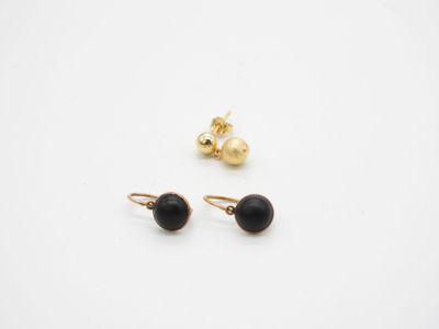 une paire de boucles d'oreilles noires et dorées posées sur une surface blanche