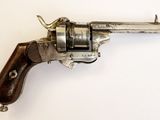 un vieux revolver en argent avec une crosse en bois, posé sur une surface blanche