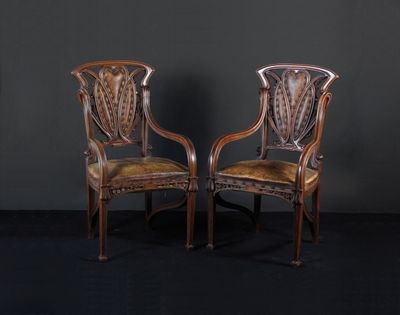 une paire de chaises anciennes aux assises recouvertes de cuir, posées devant un mur noir